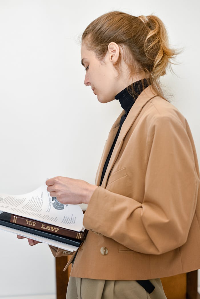 Brunette woman in brown coat reading a law book indoors.